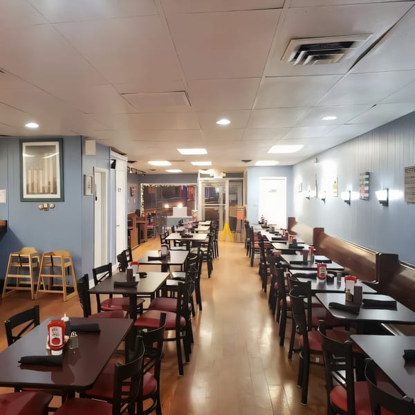 Interior of B-UNOS restaurant with rows of empty tables and chairs, light blue walls, and wood floors.