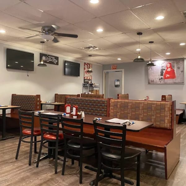 Interior of B-UNOS restaurant with booth seating, tables, chairs, and wall-mounted TVs.