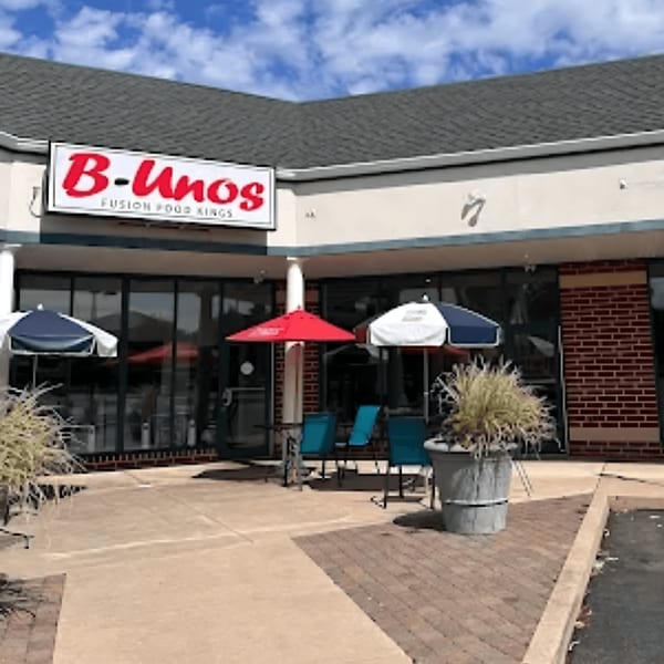 The B-Unos restaurant exterior with a red sign, outdoor seating, and umbrellas under a blue sky.