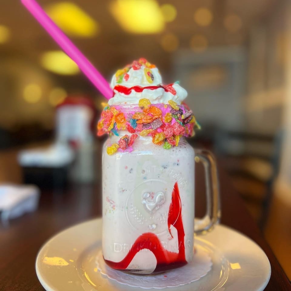 A B-UNOS milkshake in a mason jar, topped with whipped cream, syrup, and colorful cereal.