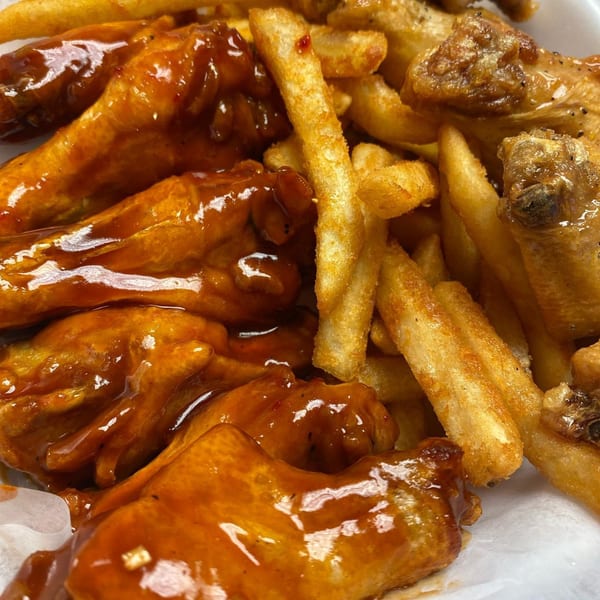 Close-up of B-UNOS' American-style chicken wings, some coated in barbecue sauce, served with golden french fries.
