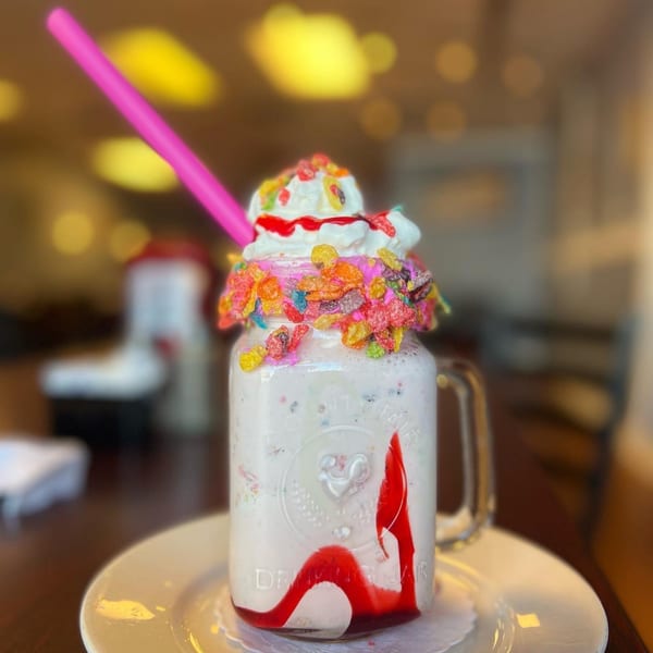 A B-UNOS milkshake in a mason jar, topped with whipped cream, colorful cereal, and a pink straw.