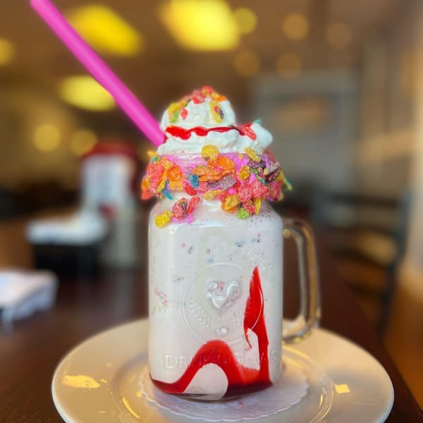 A B-UNOS milkshake in a mason jar, topped with whipped cream, colorful cereal, and strawberry drizzle.